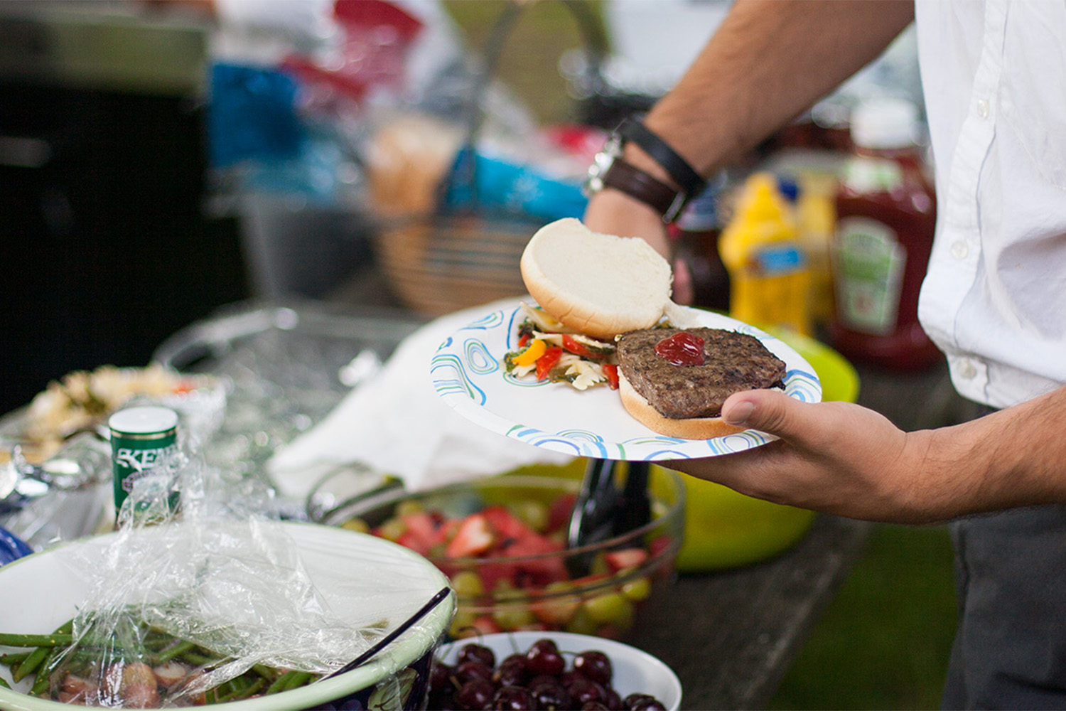 man puts ketchup on his burger by a picnic table