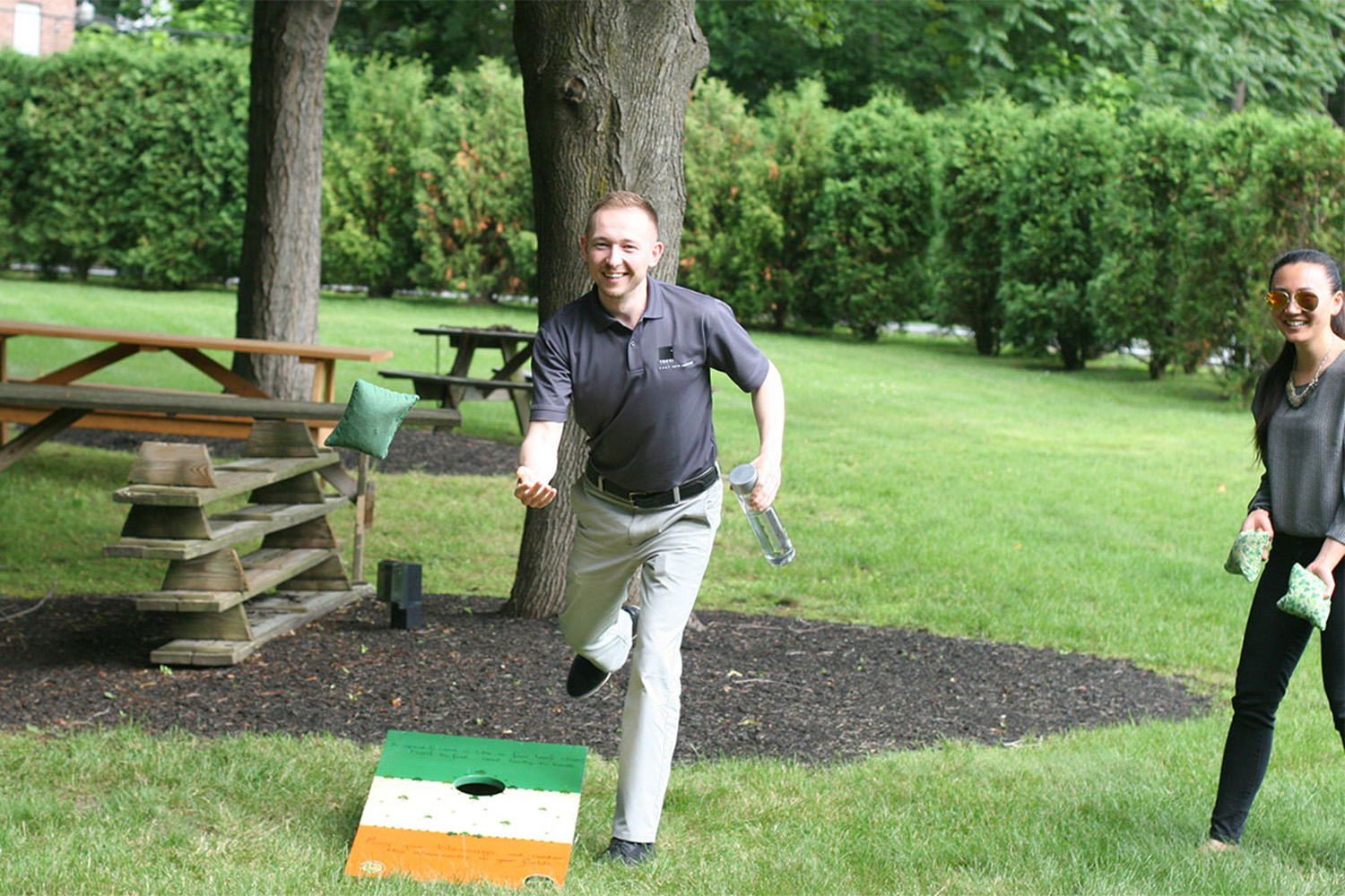 woman watches man throw sack in cornhole game 