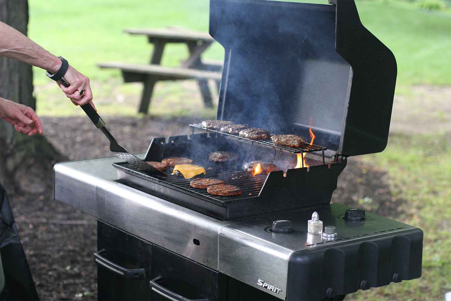 laying cheese slices on top of burgers on the grill 