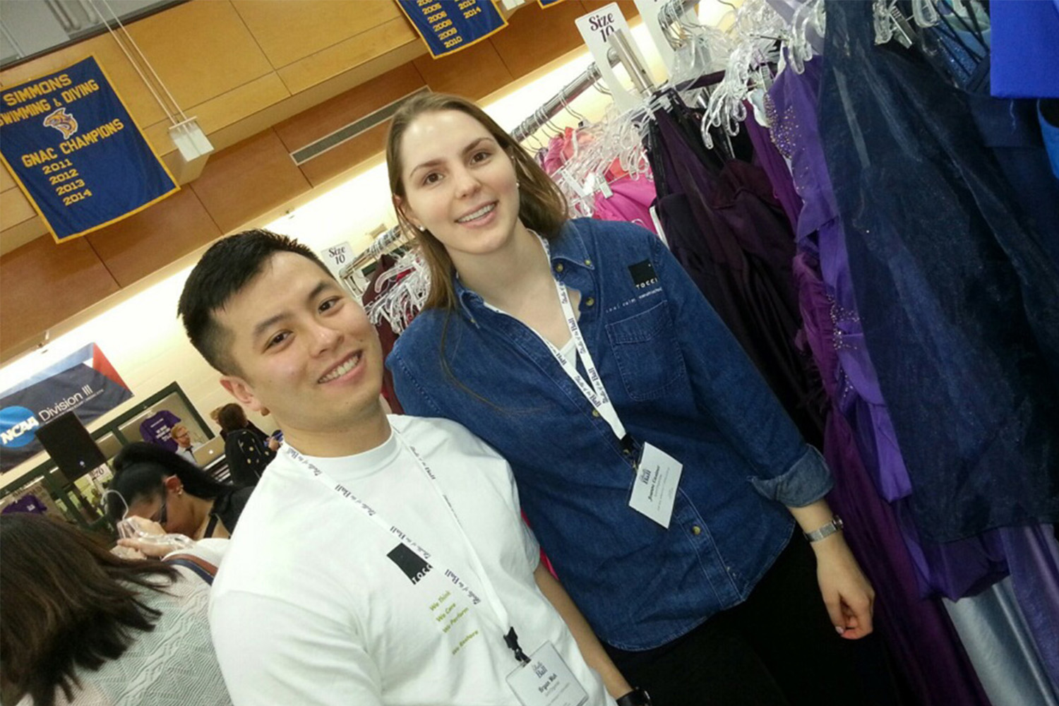 Joanne Castner and Bryan Mah pose for photo between dress racks 