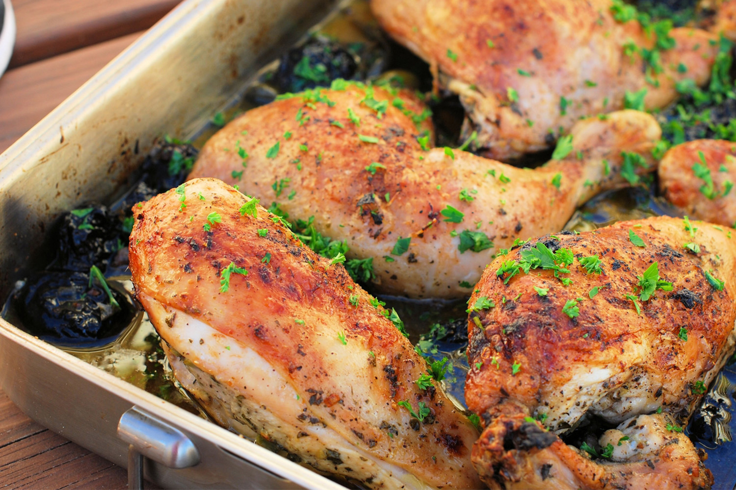 Chicken Marbella in a silver pan, with parsley sprinkled on top