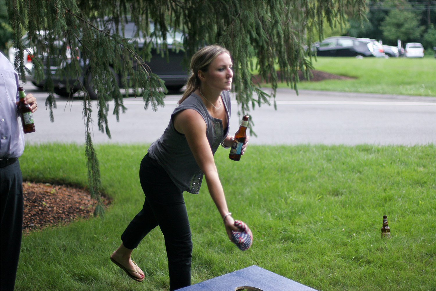 woman is leaning down, preparing to throw a sack into the cornhole 