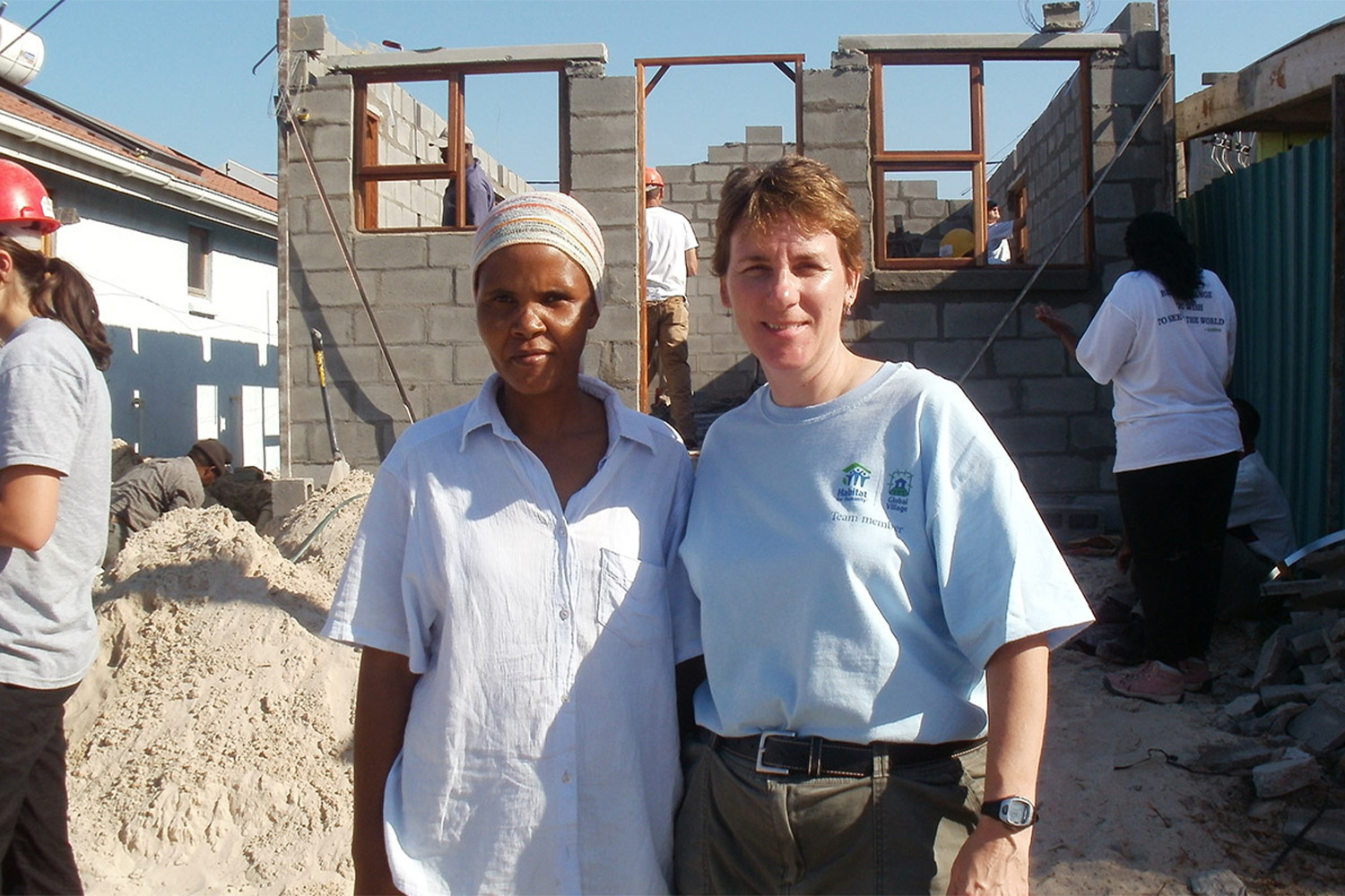 Johan on her trip to South Africa, standing with African woman outside of house under construction 