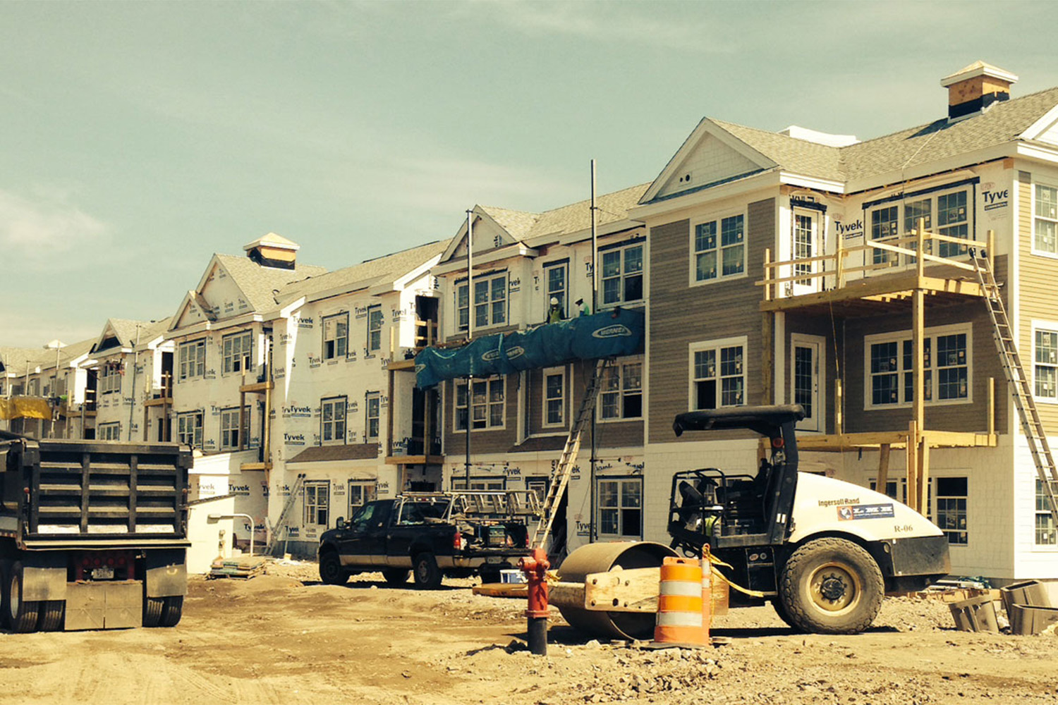 row of housing complexes under construction, with utility vehicles parked in the front