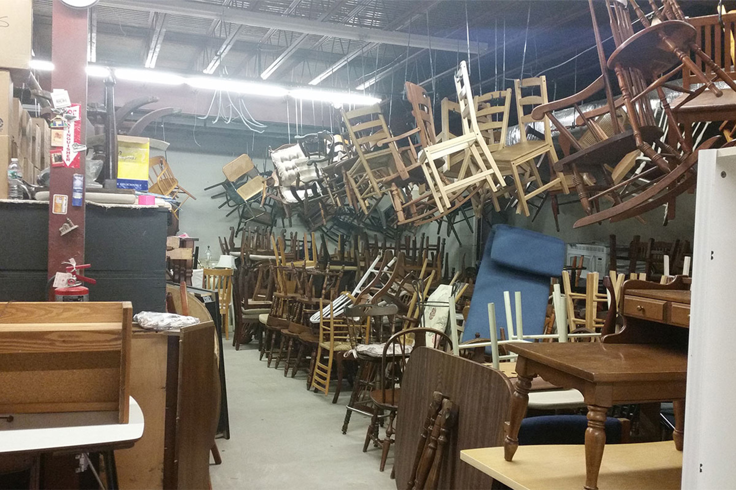 Inside the MOD warehouse: lots of wooden chairs hanging from the ceiling 