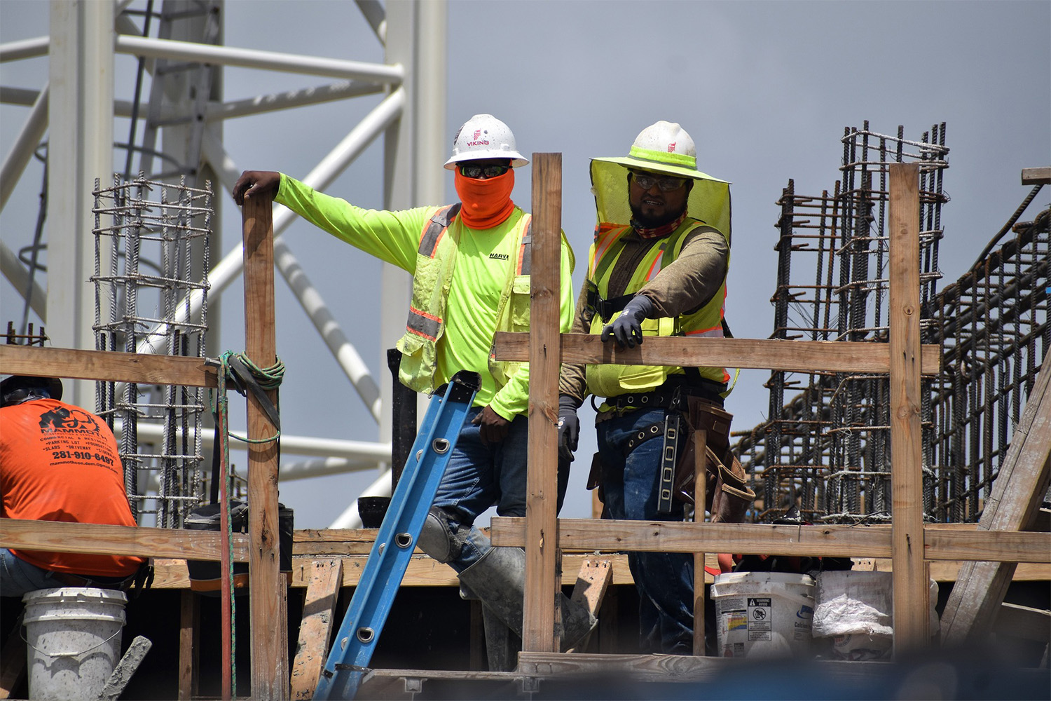 Two construction workers wearing PPE at construction site, next to ladder 