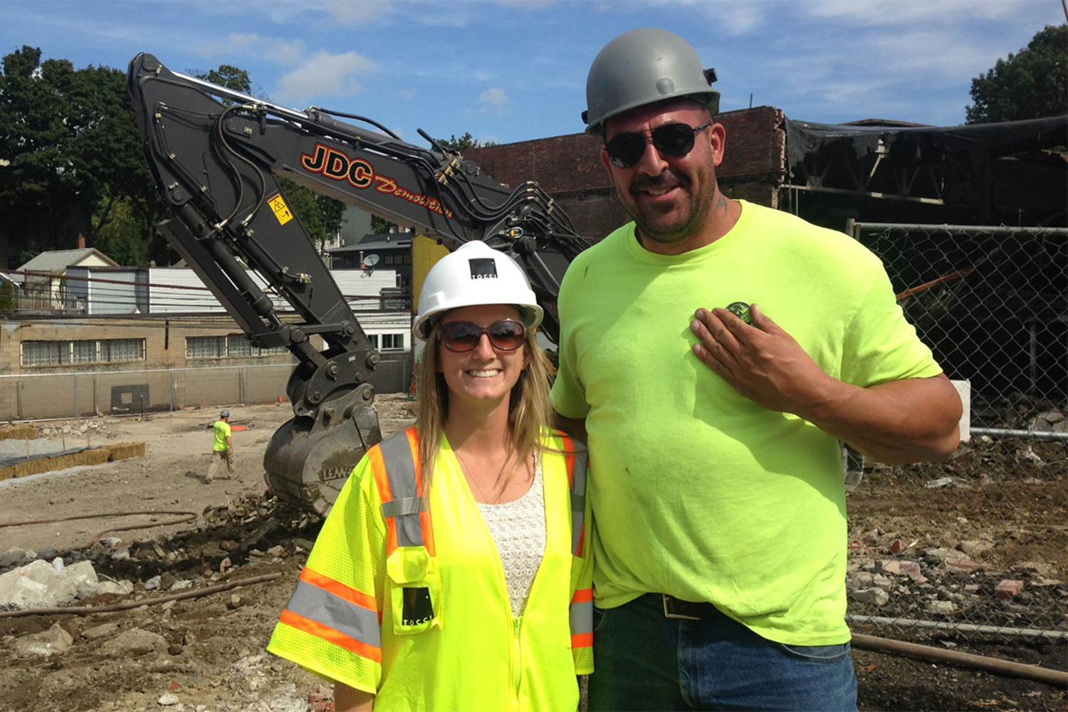 a man and woman in safety vests, taking photo in front of construction site