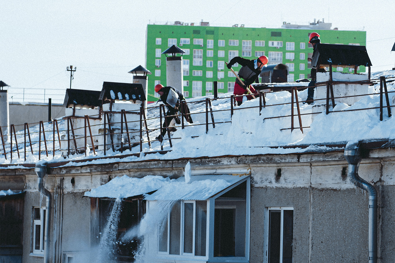 construction workers shoveling snow off of a roof