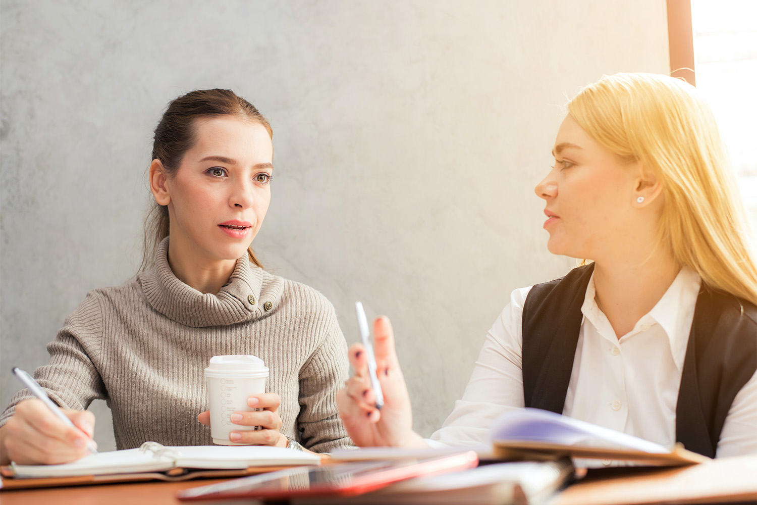 two women talking in front of window with sunshine peering through 