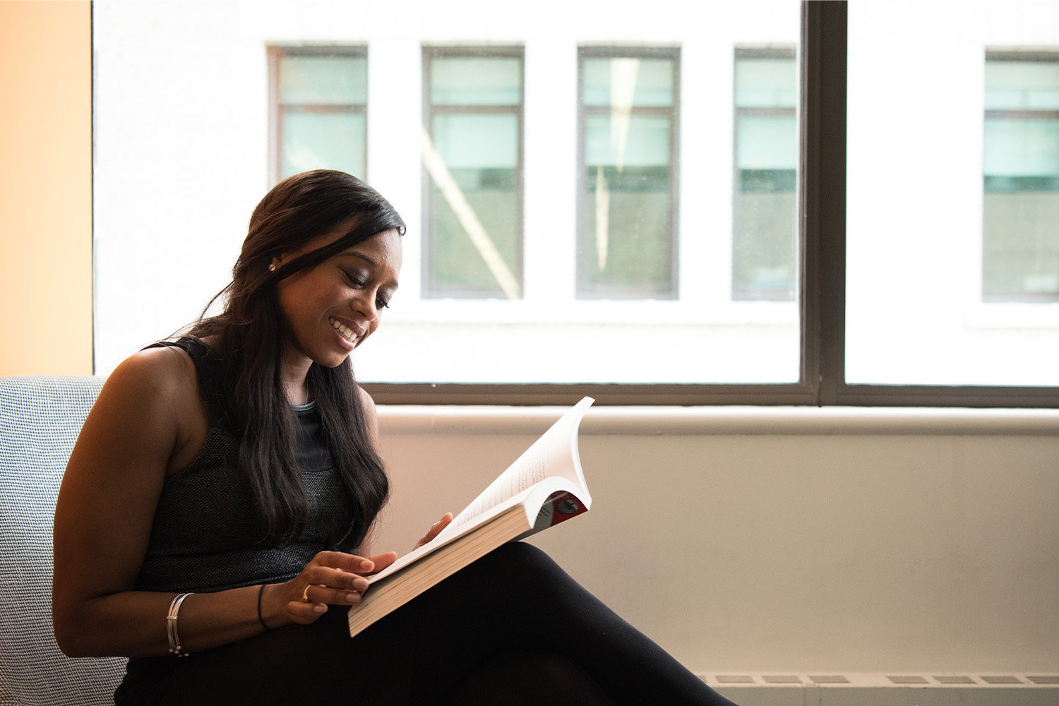 An African American woman reading a book by window sill 