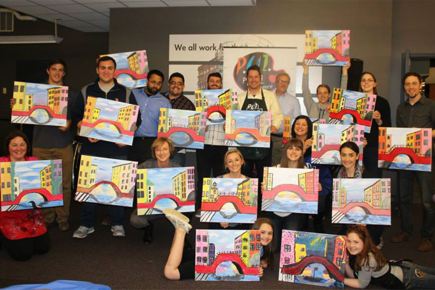 Tocci employees pose for group photo while holding up paintings 