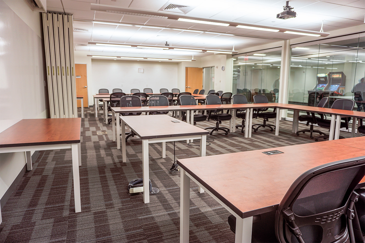 conference room area with several long wooden tables faced in front of a monitor 