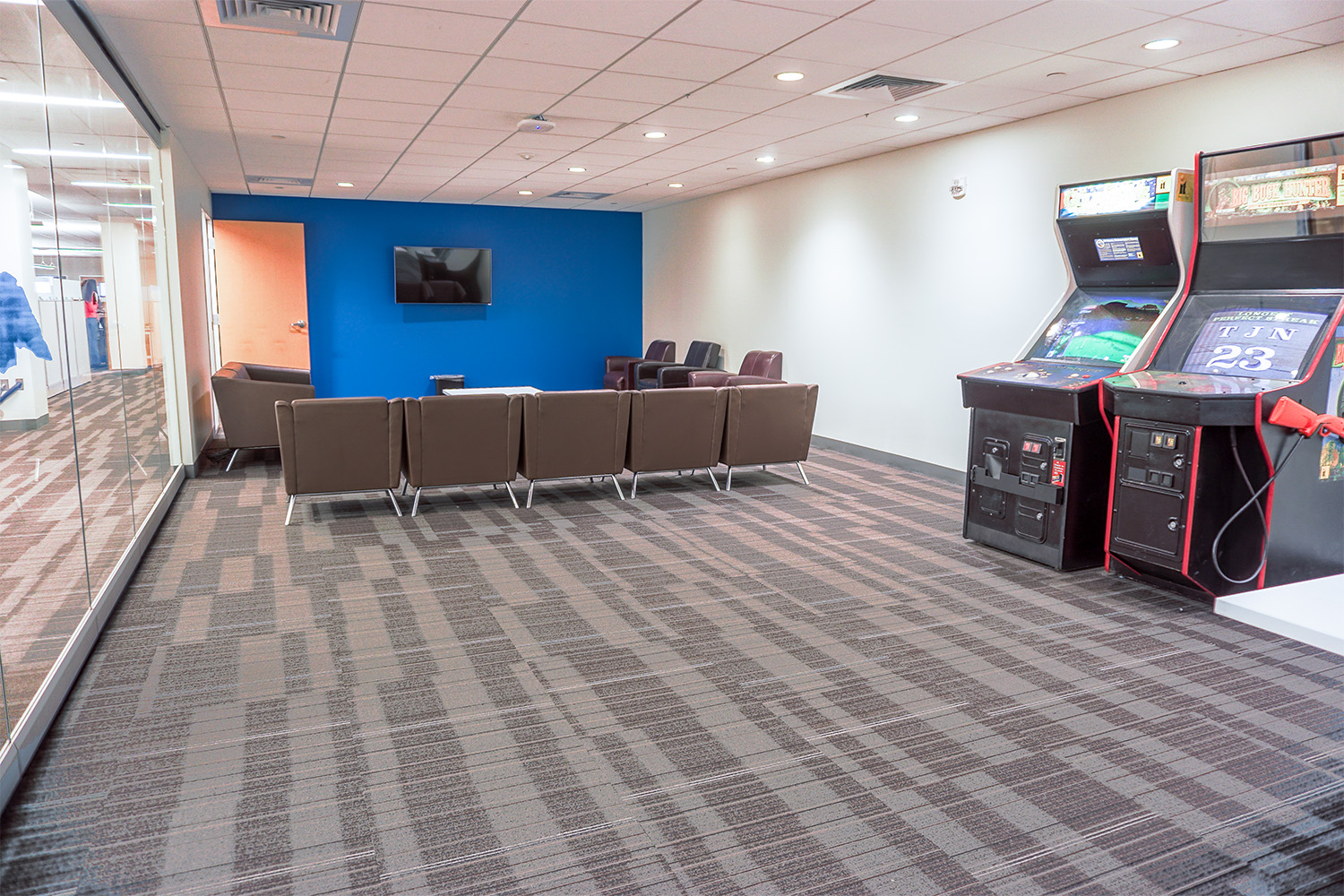 several grey chairs positioned in front of TV, and arcade games to the side 