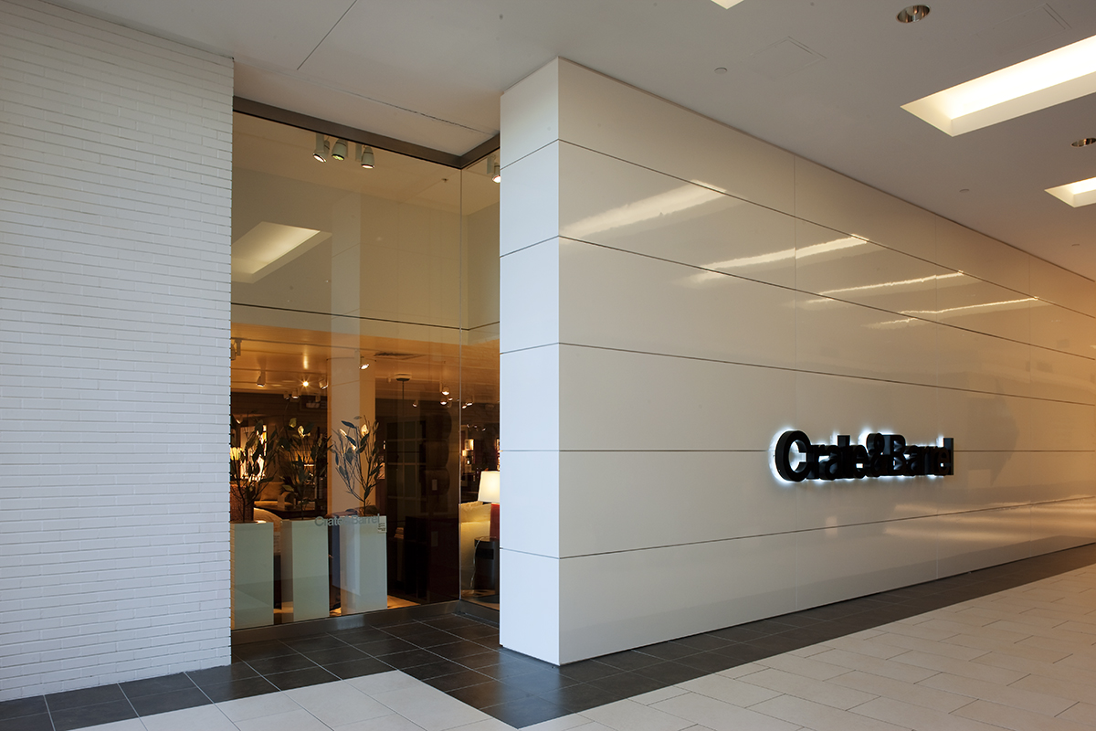 a Crate & Barrel storefront entrance in a shopping mall, with a backlit logo sign and a glass-fronted display of furniture and décor.