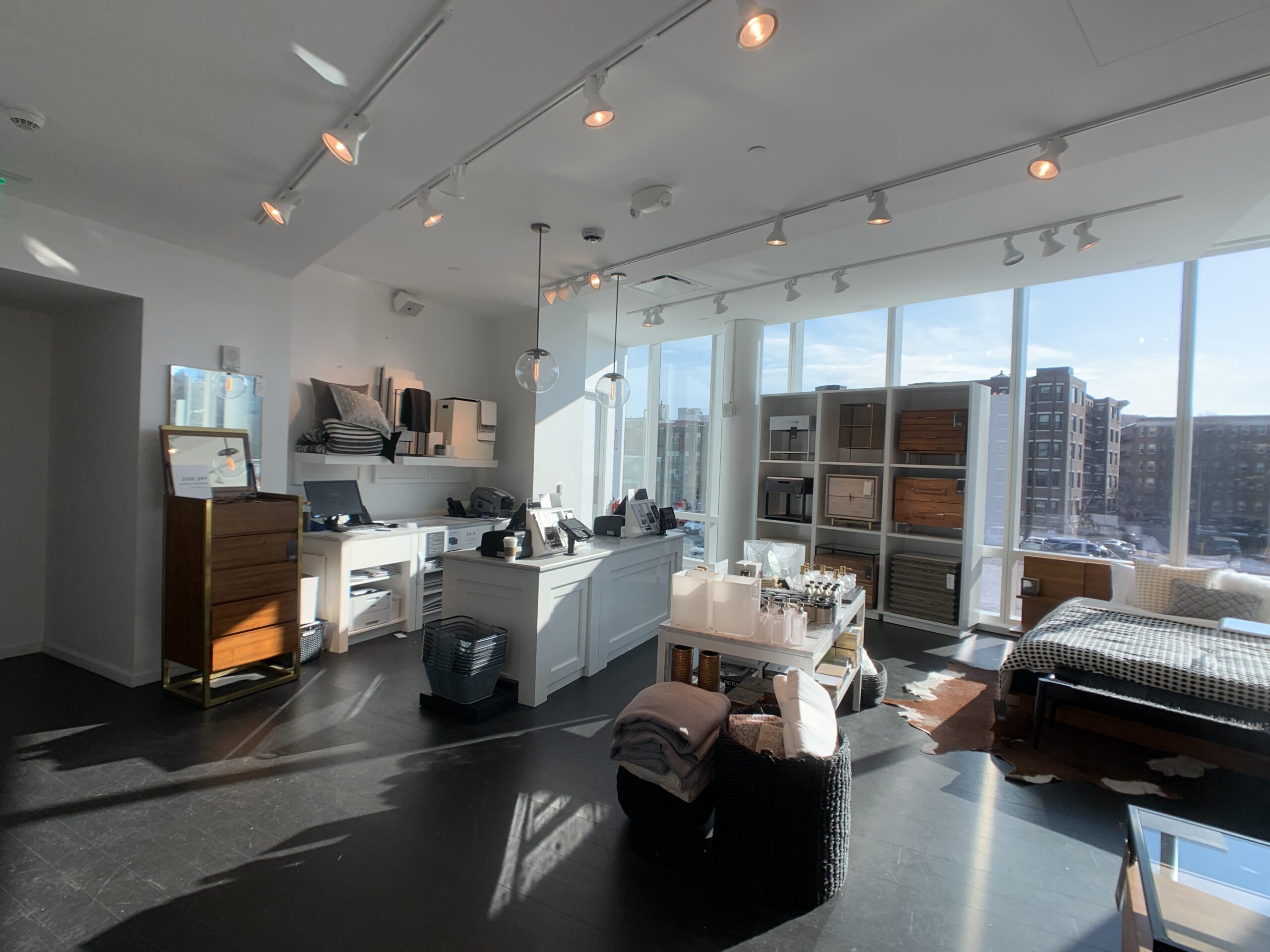 Photo of a furniture and home goods store interior with a white checkout counter, display shelving of dressers and décor, and floor-to-ceiling windows overlooking a city street.