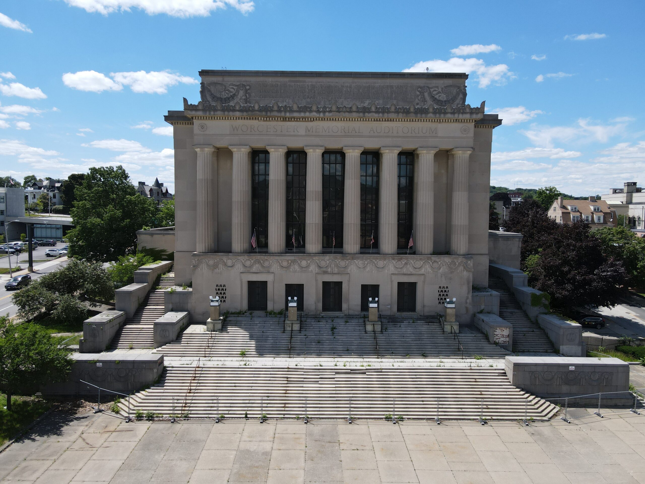 Front facade of a neoclassical stone building with tall fluted columns, arched windows, decorative frieze carvings, and a wide staircase leading up to the entrance